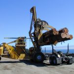 Large vehicle with claws loading logs on a truck.