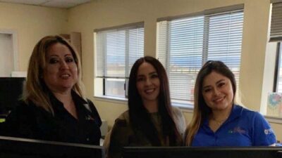 Three women in front of a computer screen smiling