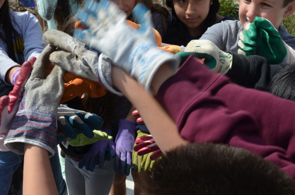 Children's hands in a circle with gloves on.