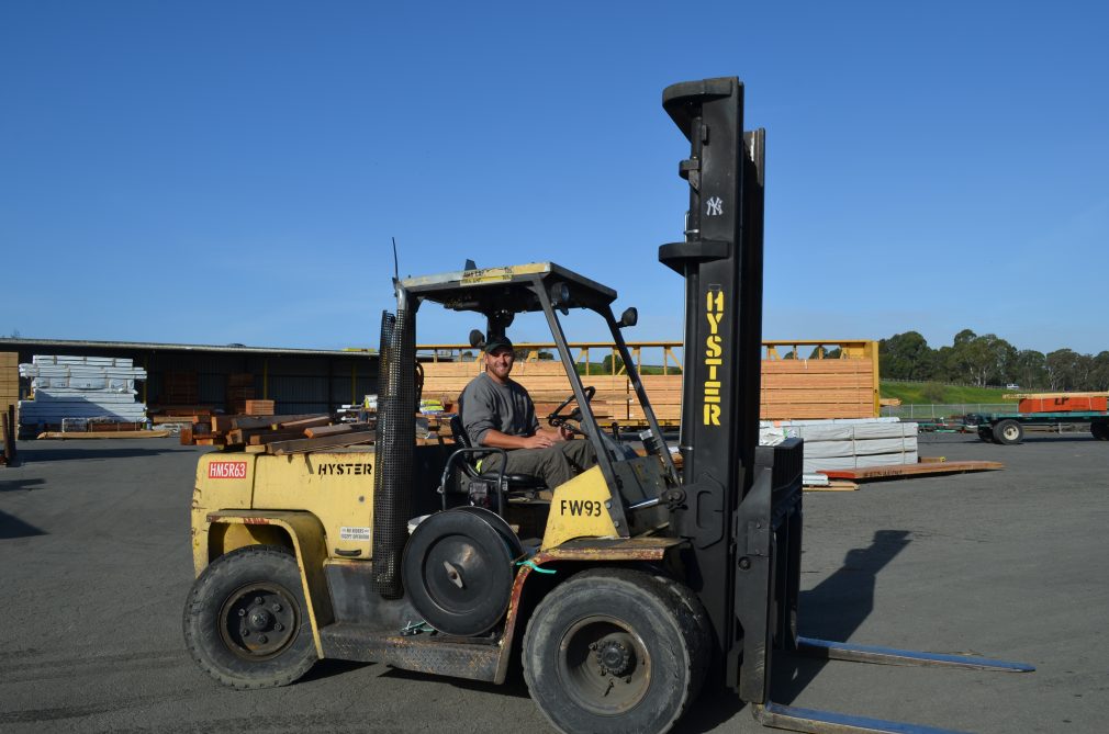 Man sitting on forklift in front of a stack of lumber