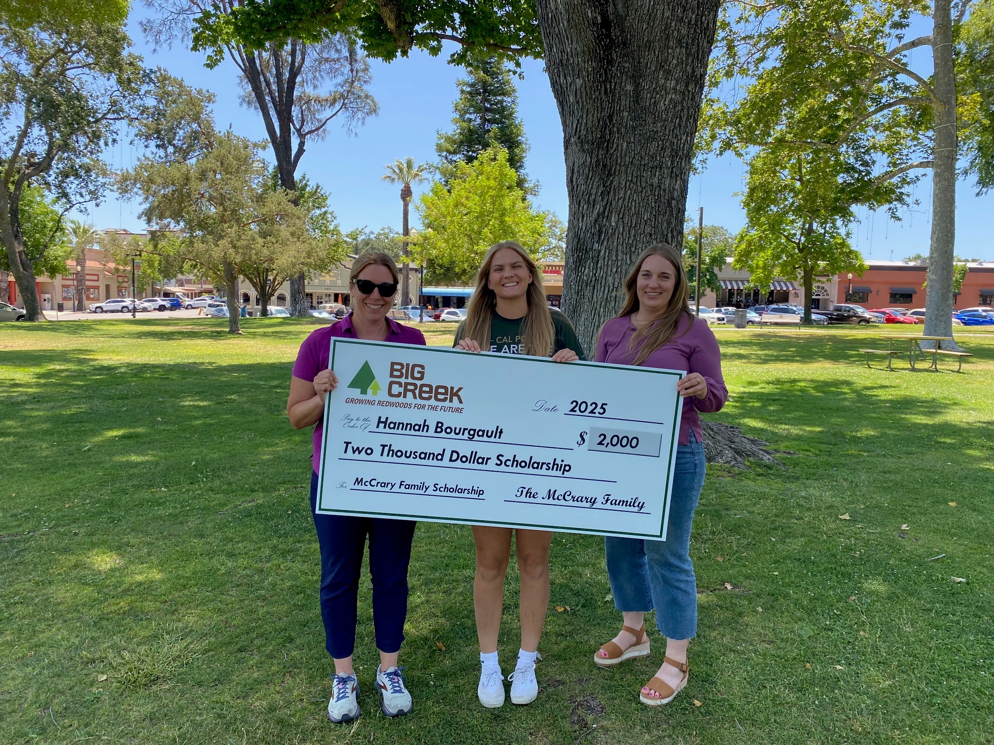 scholarship recipient holding a big check with big creek lumber representatives