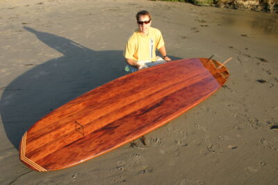 Man with redwood surfboard on the beach