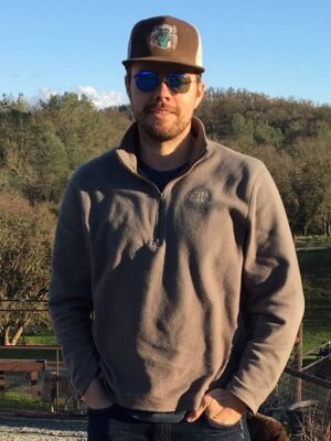 Man standing with hand in pocket and greenery in the background